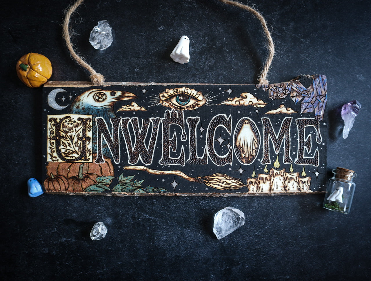 Un-Welcome door sign with spooky halloween elements including raven, mystical eye, ghost, witch’s broom, pumpkins, candles, crystals, and clouds — woodburned by Smokecraft Hollow