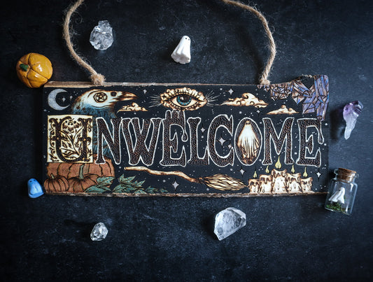 Un-Welcome door sign with spooky halloween elements including raven, mystical eye, ghost, witch’s broom, pumpkins, candles, crystals, and clouds — woodburned by Smokecraft Hollow